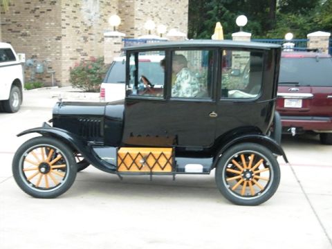 1909 Ford Model T - This antique car has a distinctive diamond-patterned box on its side, and a driver visible through the windows.