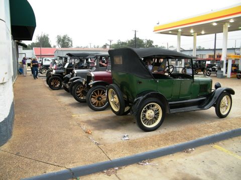 1909 Ford Model T - A line of vintage cars, including a green 1909 Ford Model T, are parked near a gas station.