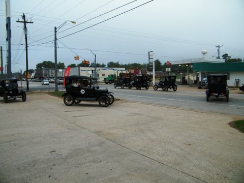 1909 Ford Model T - A convoy of vintage Ford Model T cars cruises down a street near a gas station.