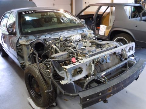 2001 Ford Crown Victoria - A disassembled 2001 Ford Crown Victoria sits in a garage, revealing its engine and front-end structure.