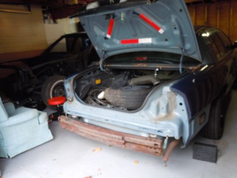 2001 Ford Crown Victoria - The rear of a Ford Crown Victoria is shown with its trunk open, revealing a spare tire and other components. Another vehicle is partially v…