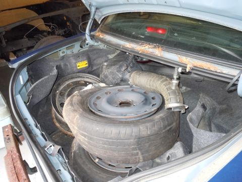 2001 Ford Crown Victoria - The trunk of a car contains spare tires and an air intake hose, with another vehicle's frame visible in the background.