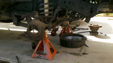1997 Dodge 3500 - Front suspension and brake assembly disassembled and supported by jack stands, with an oil pan nearby.
