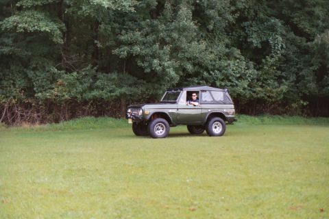 1976 Ford Bronco - 1976 Ford Bronco parked in a grassy field with trees behind it.