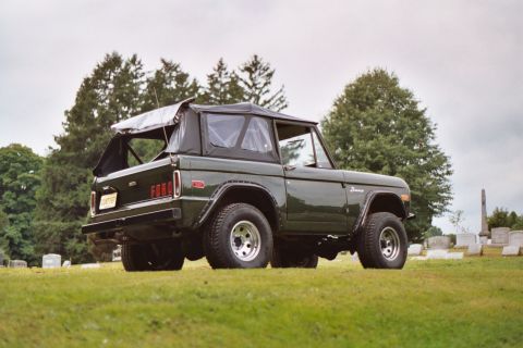 1976 Ford Bronco - Rear view of a 1976 Ford Bronco, parked outdoors in a grassy area with trees and gravestones.