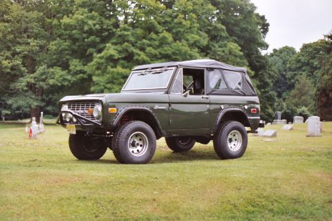 1976 Ford Bronco - A 1976 Ford Bronco sits in a grassy field with trees and gravestones in the background.