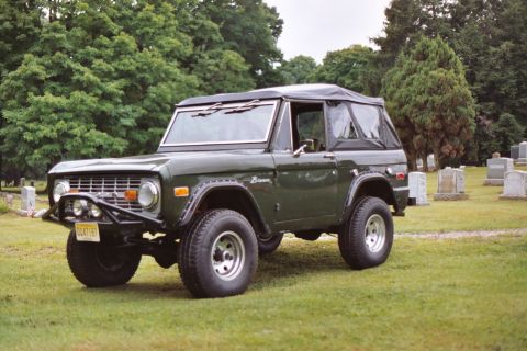 1976 Ford Bronco - This 1976 Ford Bronco is seen in a three-quarter front view, parked on a grassy area with gravestones in the background.