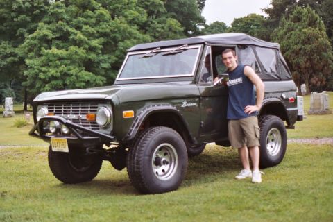 1976 Ford Bronco - A man stands next to a dark green 1976 Ford Bronco, which has a soft top and an aftermarket front bumper.