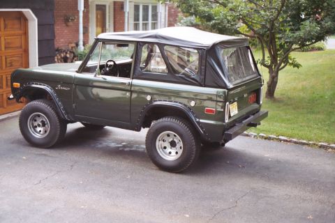 1976 Ford Bronco - 1976 Ford Bronco in dark green with a black soft top, parked in front of a house.