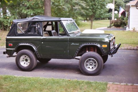 1976 Ford Bronco - This classic SUV features a dark green exterior and a black soft top, with prominent fender flares.