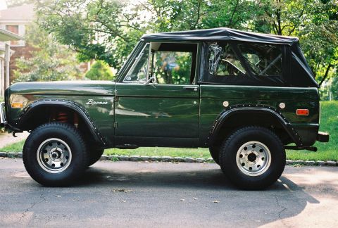 1976 Ford Bronco - A dark green 1976 Ford Bronco is parked on a street, showing its side profile with a black soft top.