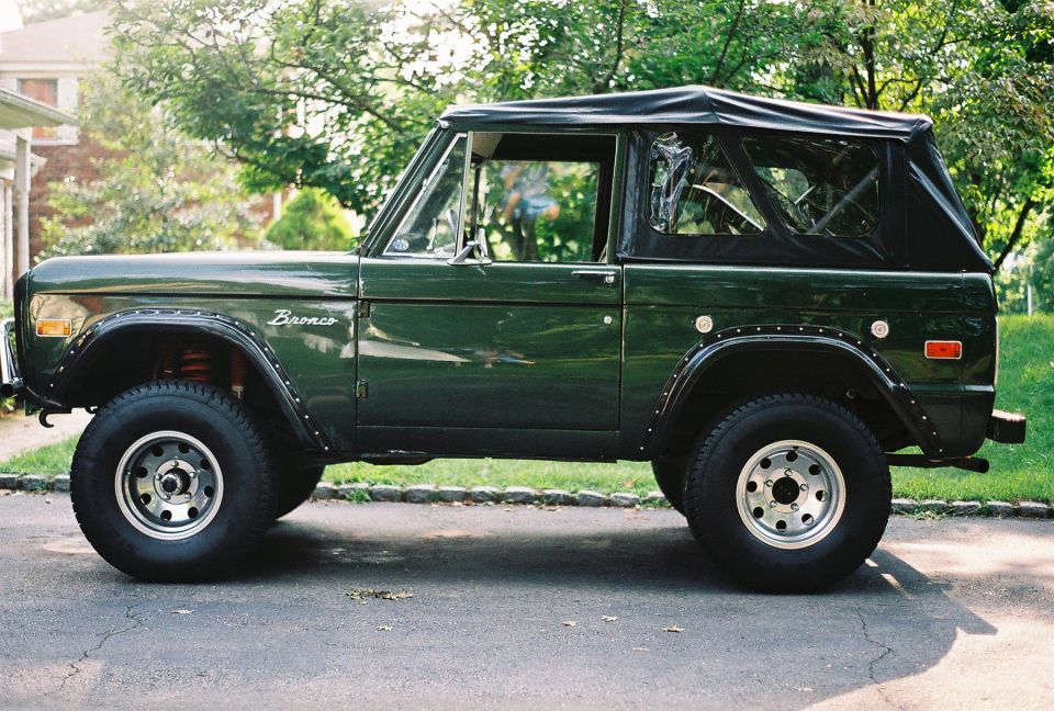 Green 1976 Ford Bronco with a black soft top, side view, parked on asphalt