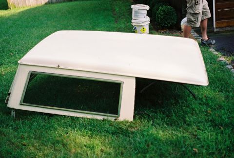 1976 Ford Bronco - A white camper shell is resting on a grassy lawn, detached from a vehicle.