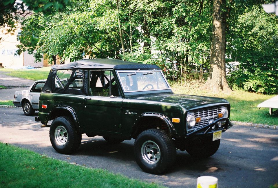 Green Ford Bronco parked on a street, another car behind it