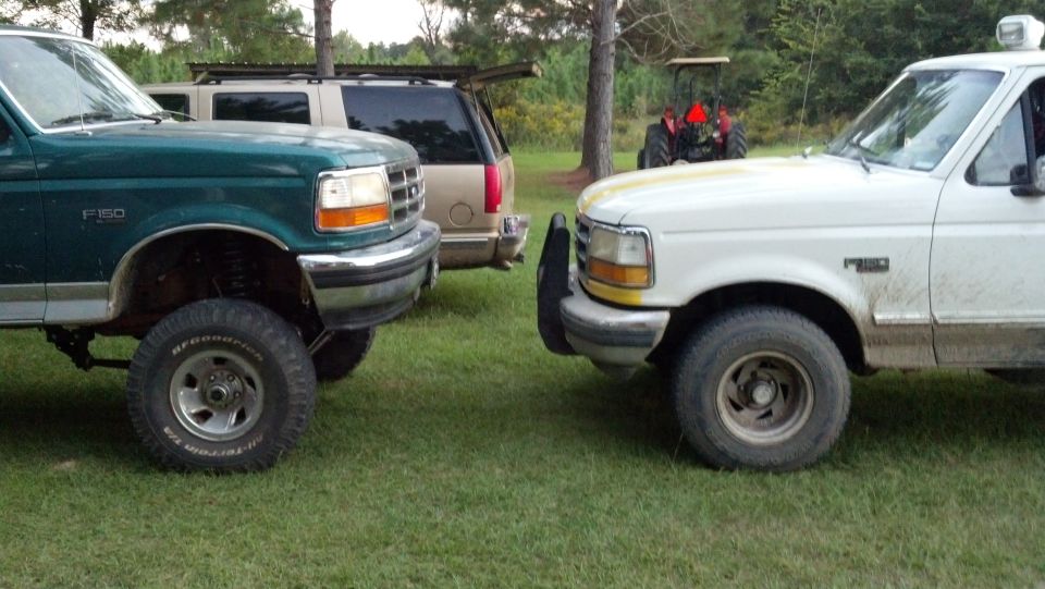 Green Ford F-150 and white Ford F-150 parked facing each other, tan SUV and tractor in background