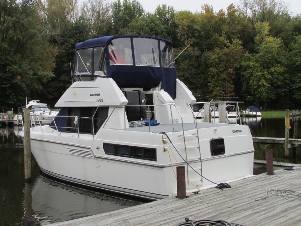 White Carver 350 boat docked at a wooden pier, rear view, with blue canvas covering the upper deck