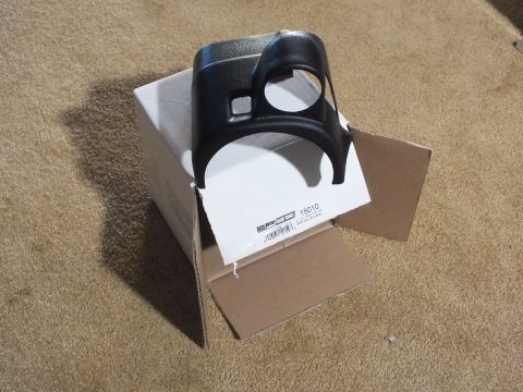 2003 Ford Crown Victoria - A black textured plastic steering-column gauge pod, cut for one round gauge and a small rectangular opening, sitting on its opened Auto Met…