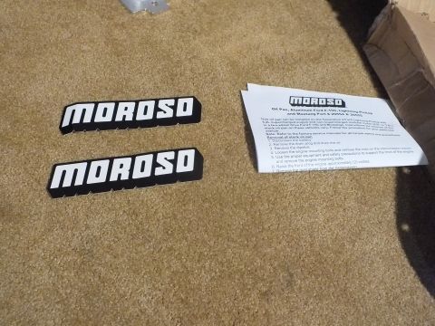 2003 Ford Crown Victoria - Two black-and-white Moroso decals laid beside a printed Moroso oil-pan instruction sheet on tan carpet.