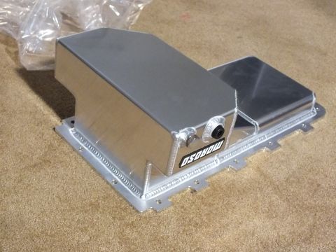 2003 Ford Crown Victoria - polished fabricated aluminum oil pan branded Moroso, with welded seams and an external fitting, sitting on tan carpet.