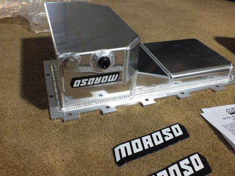 2003 Ford Crown Victoria - fabricated aluminum Moroso oil pan with welded sump and fittings, shown beside two black Moroso decals and an instruction sheet on carpet.