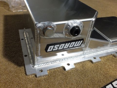 2003 Ford Crown Victoria - Close-up of a fabricated polished aluminum oil pan with welded seams, two threaded fittings, and a Moroso decal resting on carpet.