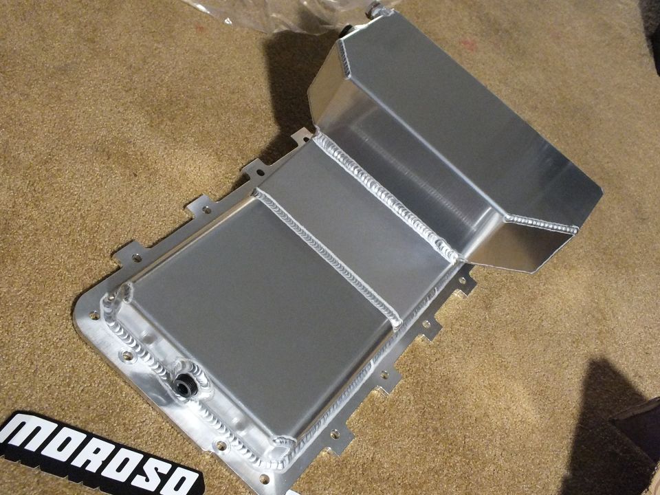Open aluminum oil pan showing internal baffle and Moroso decal on carpet