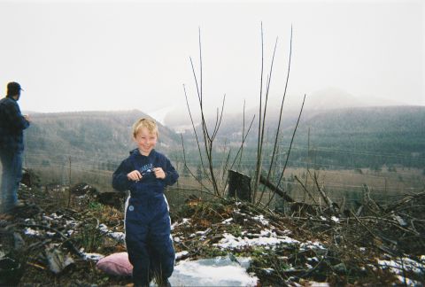 1983 Ford Bronco - A smiling child in a navy hooded sweatshirt and snow pants stands on a snow-dusted clear-cut hilltop, with an adult in a ball cap at the le…