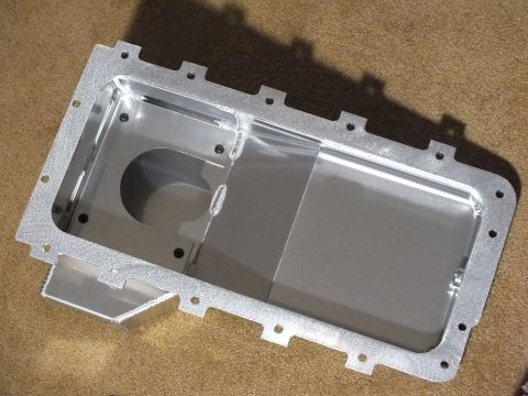 2003 Ford Crown Victoria - Top-down view into a cast-textured aluminum oil pan showing the bolt flange and a circular pickup cutout, on carpet.