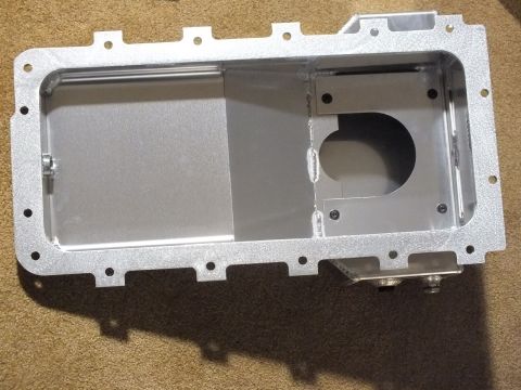 2003 Ford Crown Victoria - Top view of a cast-textured aluminum oil pan interior showing the mounting flange and a round oil-pickup cutout, on carpet.