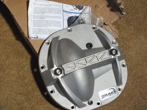 2003 Ford Crown Victoria - Cast aluminum differential cover with ribbed reinforcement and a Drake decal, mounted with hex bolts, resting in a cardboard box.