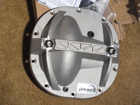 2003 Ford Crown Victoria - Front view of a cast aluminum Drake differential cover with ribbed reinforcement bar and hex hardware, on carpet with instructions.