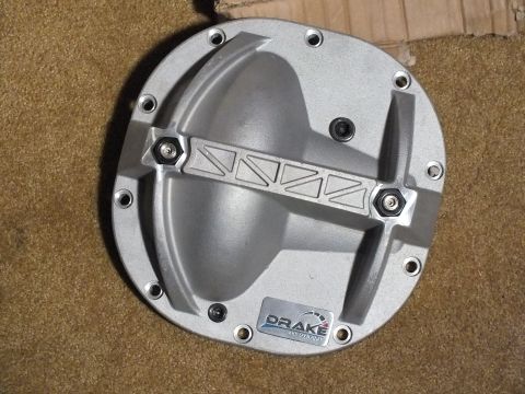2003 Ford Crown Victoria - Angled view of a cast aluminum Drake differential cover with a ribbed reinforcement bar and hex adjusters, on carpet.