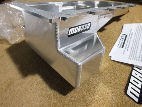 2003 Ford Crown Victoria - Side profile of a fabricated aluminum Moroso oil pan showing the welded kick-out sump, decal, and printed instructions on carpet.