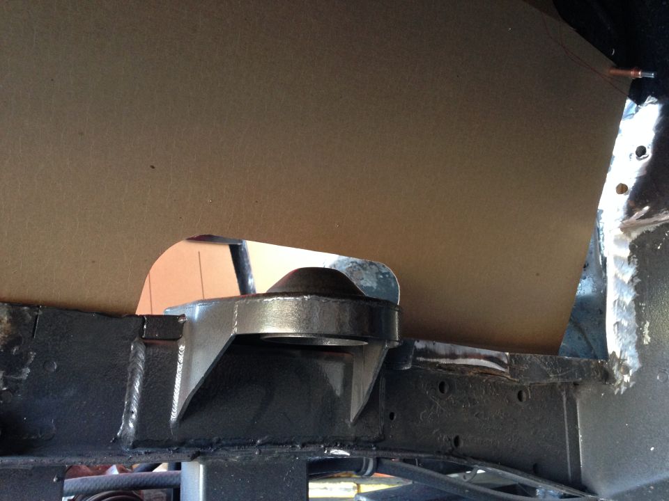 Close-up of a metal bracket bolted to a vehicle's frame, with a piece of cardboard behind it