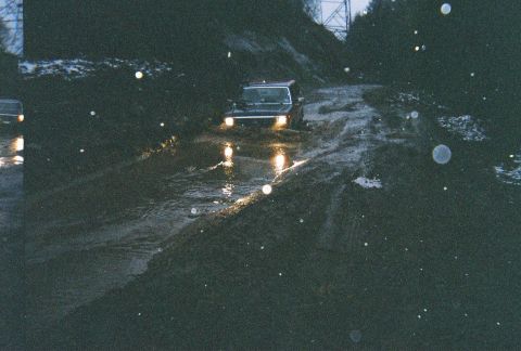 1983 Ford Bronco - Two vehicles navigate a challenging, wet, and muddy path, kicking up water and mud.