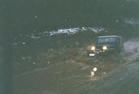 1983 Ford Bronco - A Jeep Wrangler navigates a muddy terrain with its headlights illuminated.