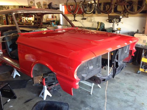 1964 Ford Fairlane - A red car body is undergoing restoration in a garage, with parts removed and the frame supported by jack stands.