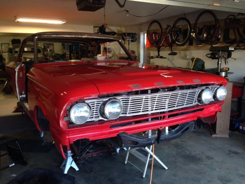 1964 Ford Fairlane - A vintage red car is undergoing restoration in a garage, supported by jack stands.