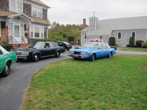 2001 Ford Crown Victoria - A blue police car is parked on the lawn in front of a church, with other vehicles nearby.