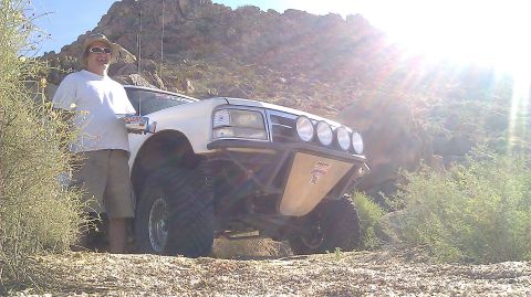 1996 Ford Bronco - A modified white Ford Bronco sits off-road with a person standing next to it in a sunny, rocky environment.
