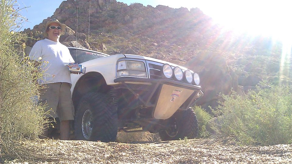White Ford Bronco with off-road tires, custom bumper, and light bar, parked on a dirt road in a desert landscape