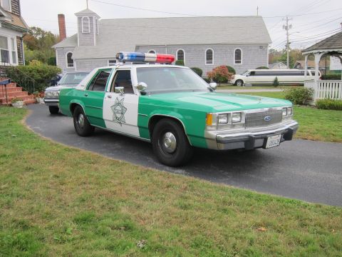 2001 Ford Crown Victoria - A vintage police car with a light bar is parked on a driveway in front of a church.