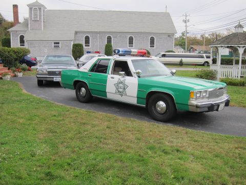 2001 Ford Crown Victoria - A green and white police car is parked on a driveway in front of a church, with a limousine visible in the background.
