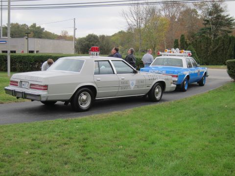 2001 Ford Crown Victoria - Two Rhode Island State Police vehicles are parked on a paved surface next to a grassy area.