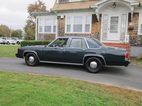2001 Ford Crown Victoria - A dark 2001 Ford Crown Victoria sedan is parked on a driveway in front of a house.