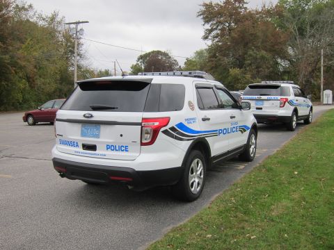 2001 Ford Crown Victoria - Two Swansea Police SUVs are parked side-by-side on a cloudy day, with trees and a telephone pole in the background.