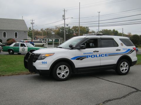2001 Ford Crown Victoria - A white police SUV is parked on asphalt, with a green and white police car in the background.