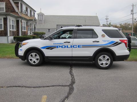 2001 Ford Crown Victoria - Side view of a white police SUV with "Swansea Police" text and emergency dial 911 markings.