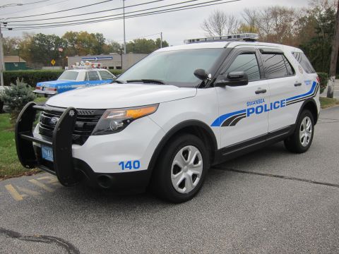 2001 Ford Crown Victoria - A white police SUV is parked next to an older blue police car. The SUV has 'SWANSEA POLICE' text on its side.
