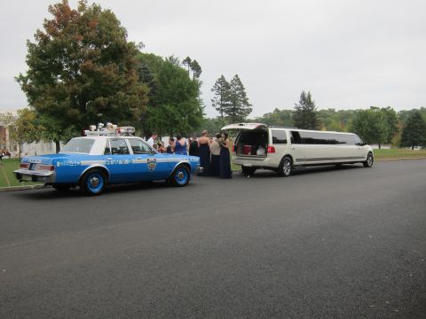 2001 Ford Crown Victoria - A vintage police car and a modern limousine are parked together on a cloudy day.